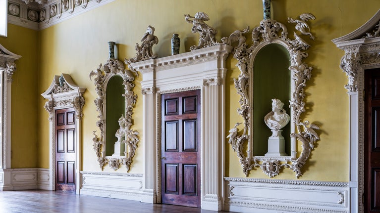 The North Hall at Claydon is decorated with yellow walls, ornate alcoves house statuary.